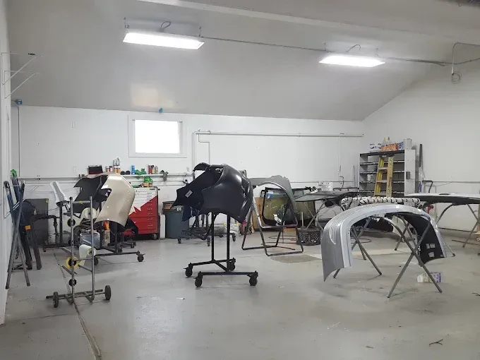 Auto body repair shop with several car parts and frames on stands in a bright workshop