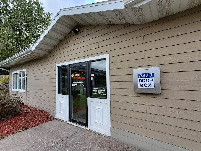 Exterior of a beige building with a glass entrance door and a blue drop box sign beside it