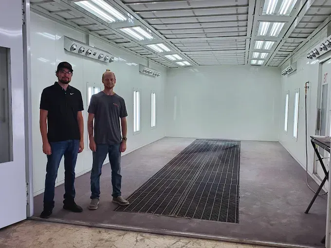 Two men standing in a bright empty room with white walls and a large black floor mat