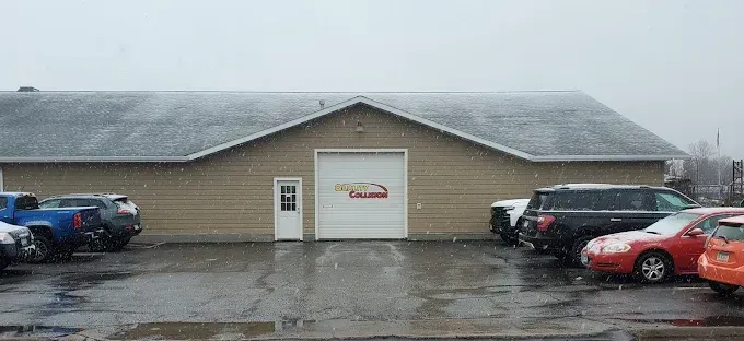 Snowy parking lot outside a beige warehouse with parked cars and a garage door