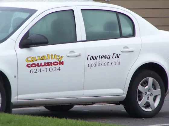 White sedan with “Quality Collision” and “Courtesy Car” business decals on the side