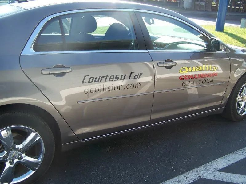 Silver Courtesa car parked on pavement with dealership logos on the doors