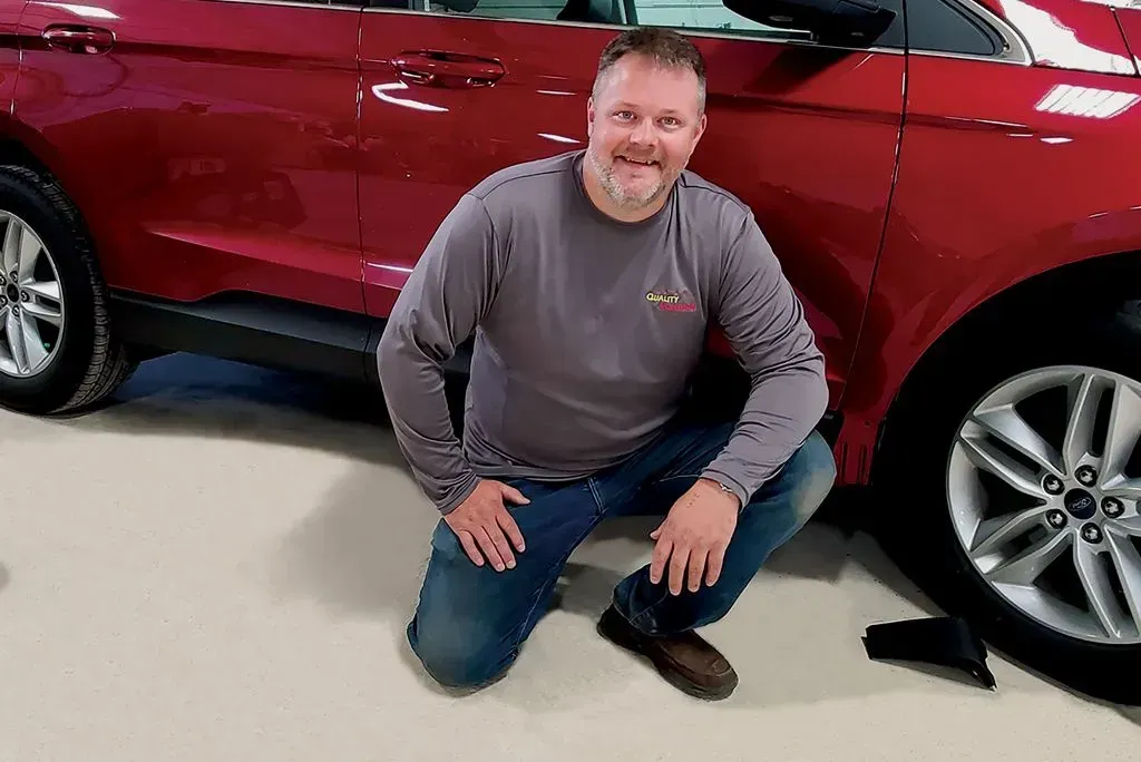 Man kneeling beside a red SUV in a garage, smiling at the camera.