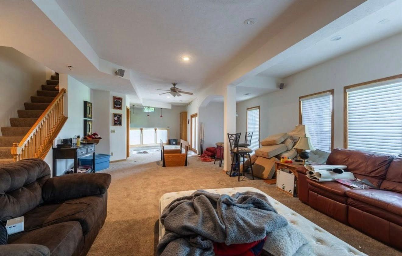 Spacious living room with brown sofas, staircase, and warm tan carpet in a bright open floor plan.