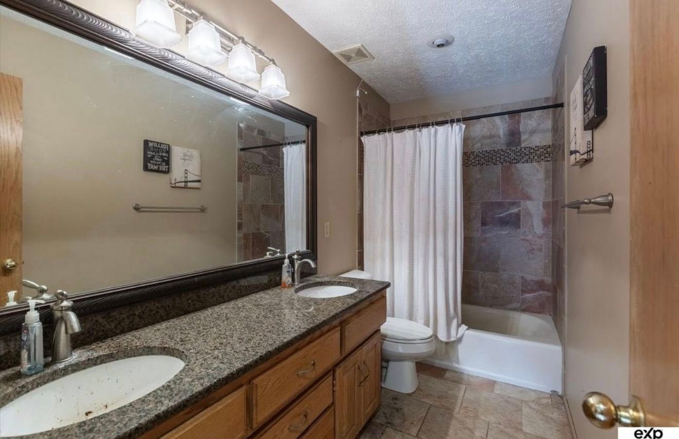 Spacious bathroom with dual sinks, large mirror, toilet, and shower with white curtain