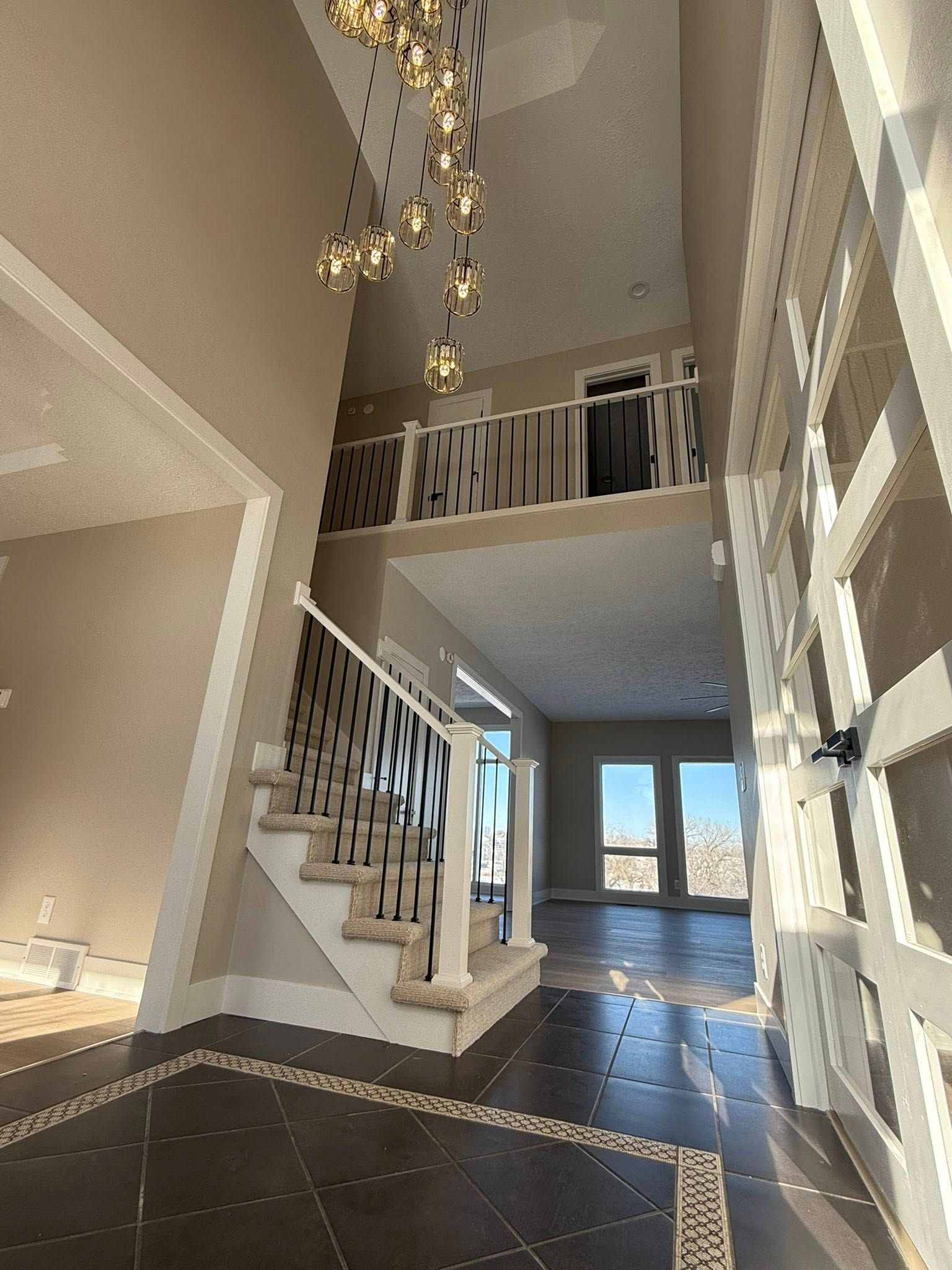 Modern foyer with high ceiling, staircase, chandelier, and tiled floor leading to a bright entryway