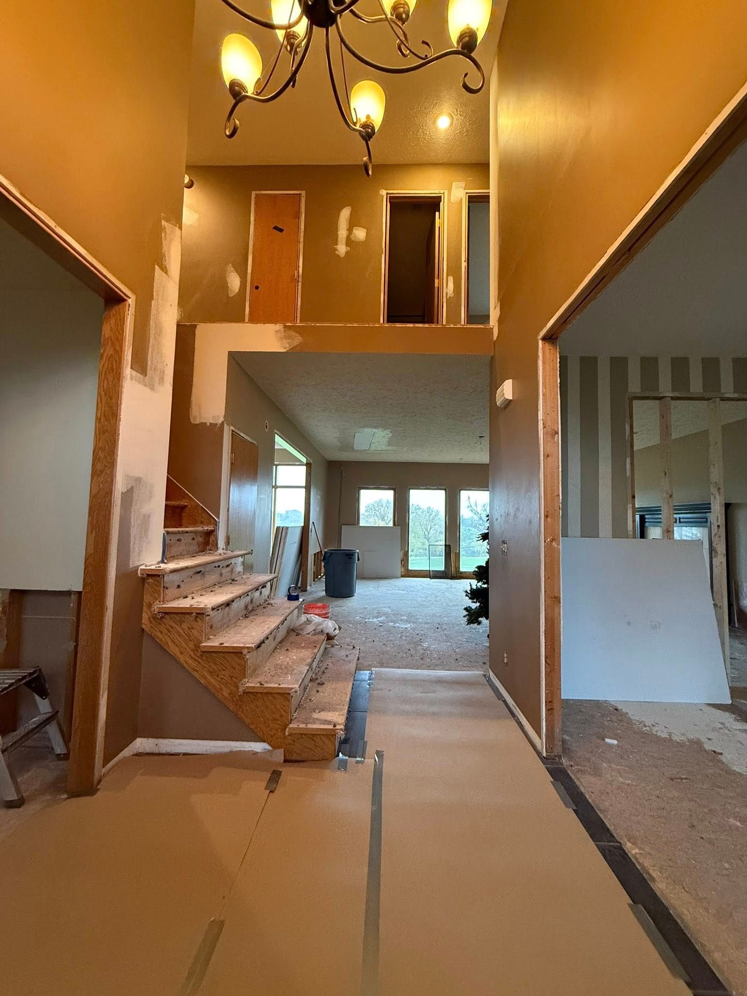 Unfinished two-story interior with stairs, exposed drywall, and hanging ceiling lights.