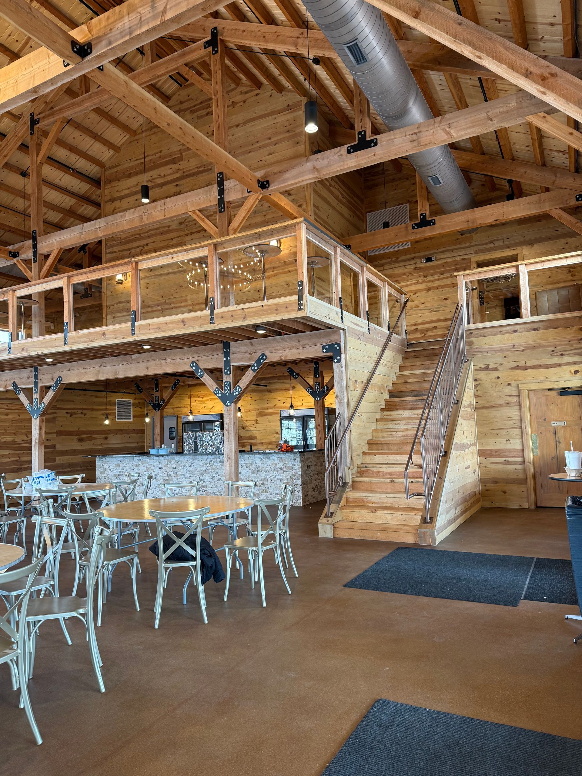 Rustic wooden lodge interior with loft, staircase, and tables set with clear chairs