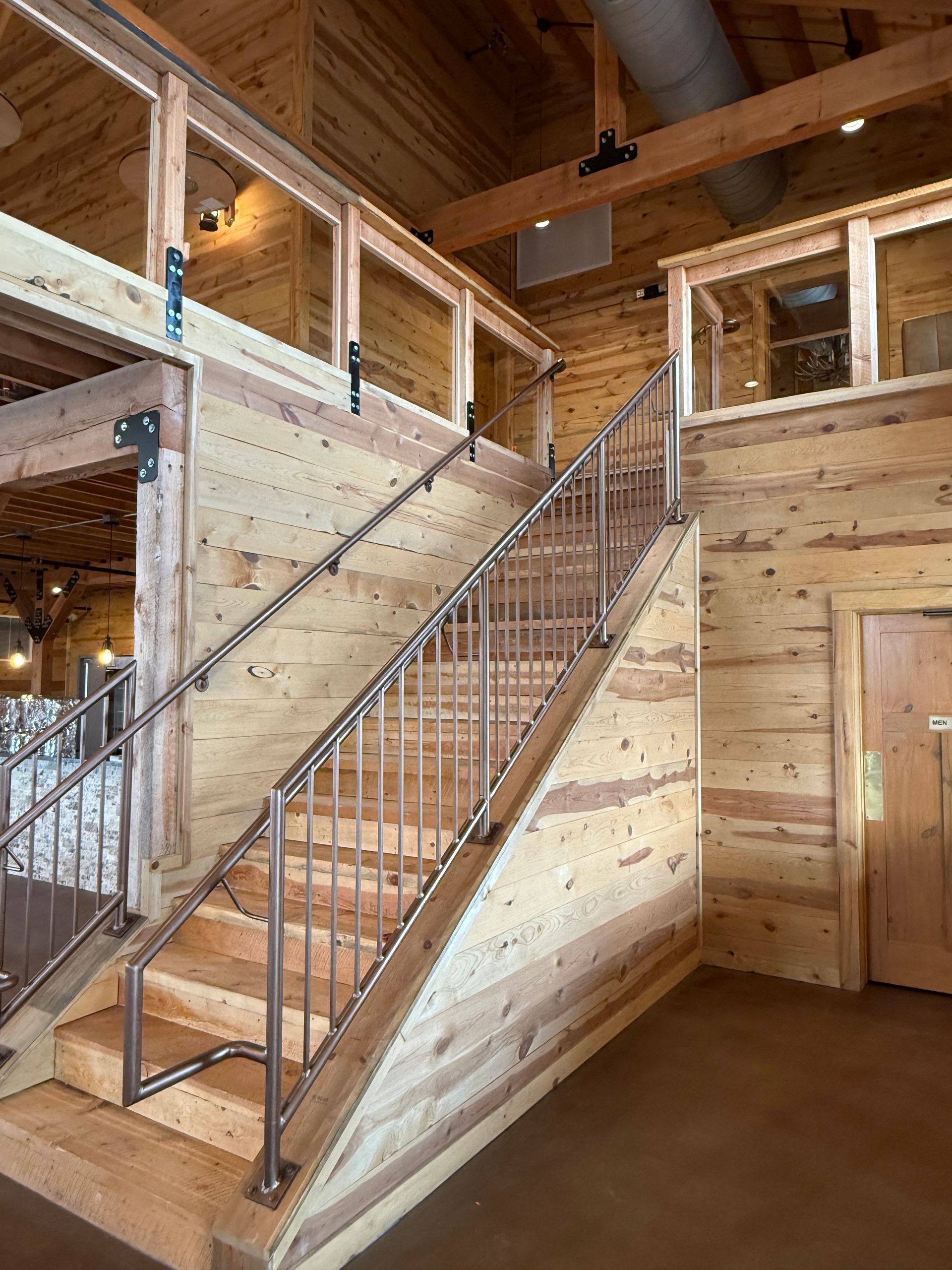 Wooden interior staircase in a loft-like cabin with exposed beams and a railing.