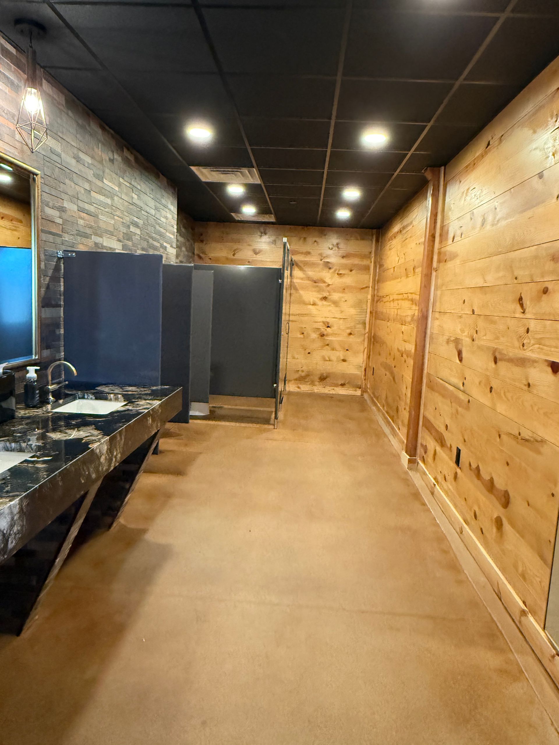 Empty industrial hallway with wood-paneled right wall, brick left wall, and dark ceiling lights