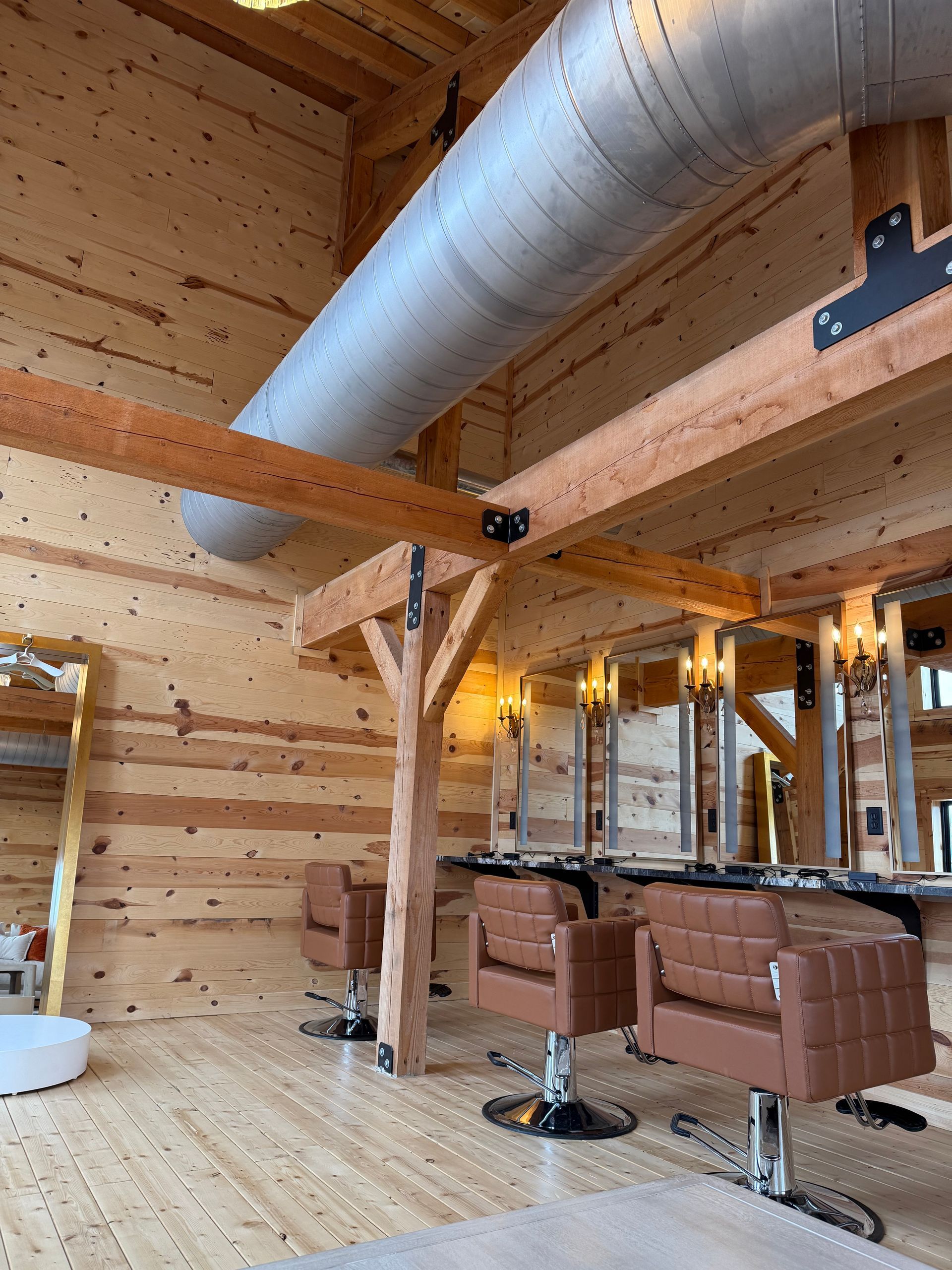 Rustic salon with wood-paneled walls, exposed ductwork, and brown styling chairs under warm lights