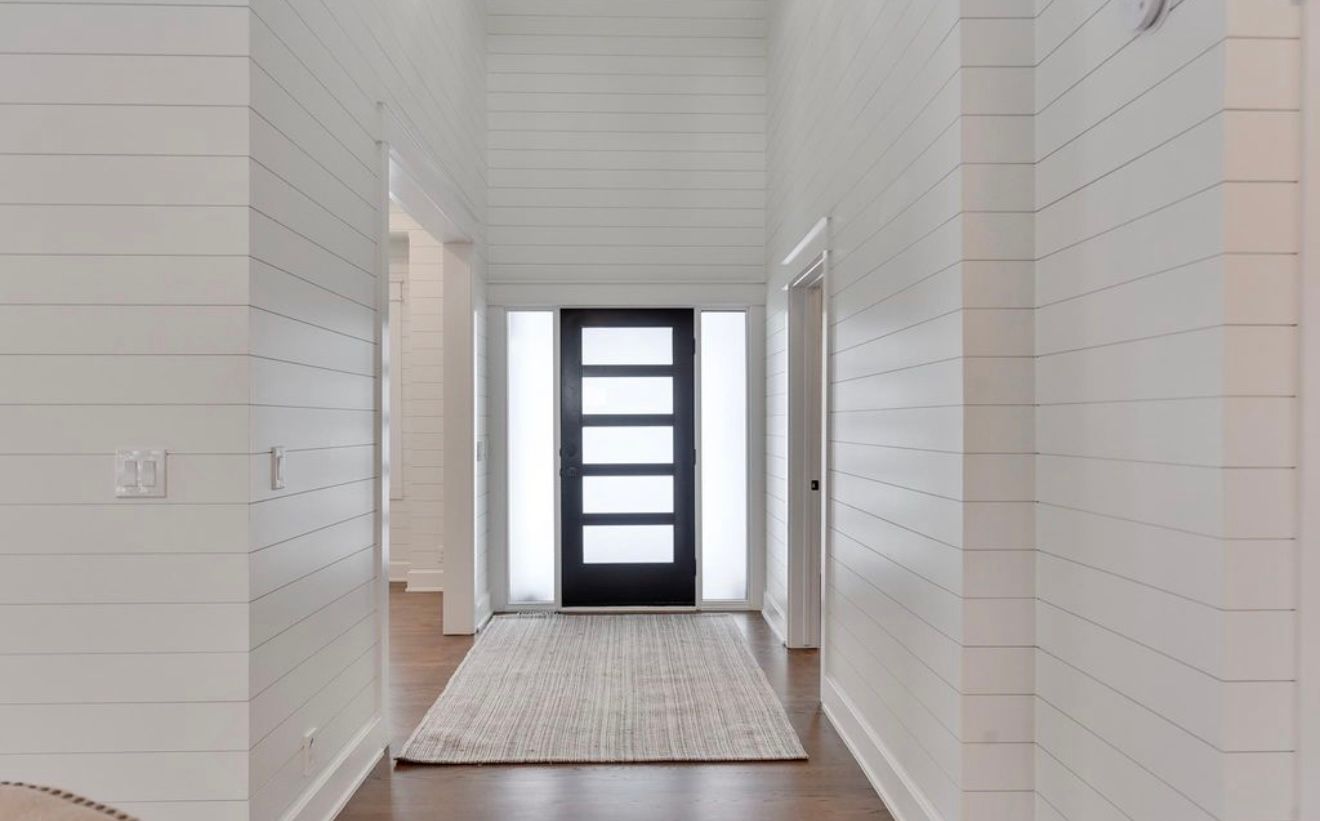Bright white hallway with wood floors, a runner rug, and a black front door at the end.