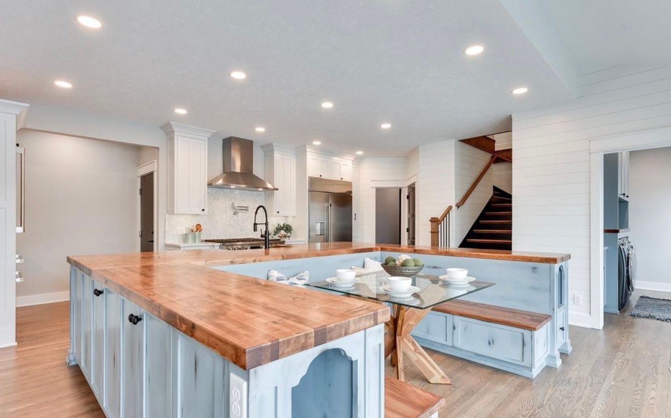 Bright open kitchen with wood island, white cabinets, stainless hood, and staircase in the background