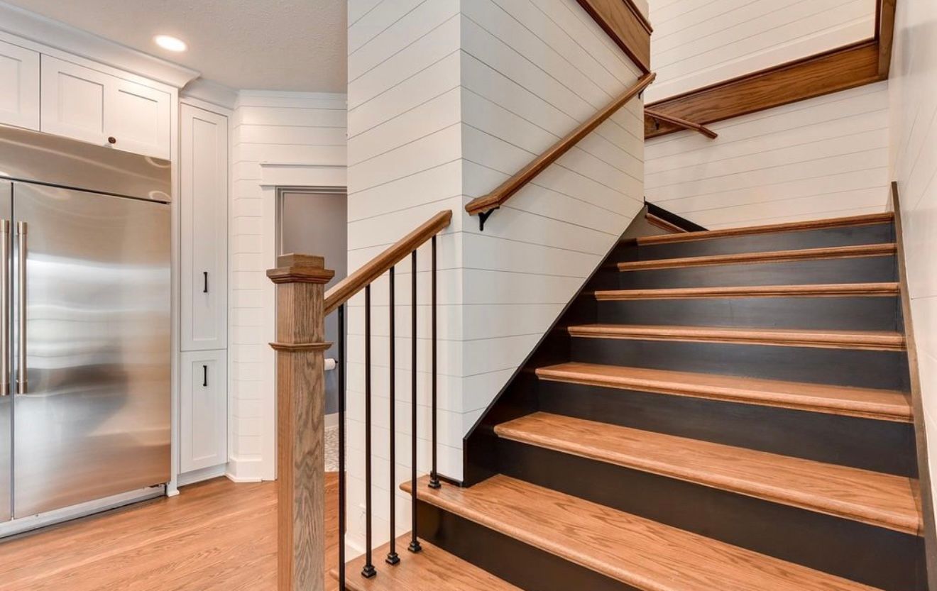 Modern kitchen stairway with dark wood steps, white walls, and stainless steel appliances