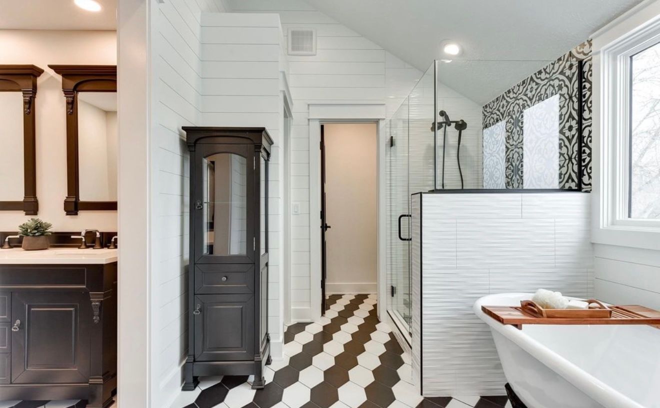 Bright white bathroom with black-striped floor, glass shower, and a dark wood cabinet near a tub.