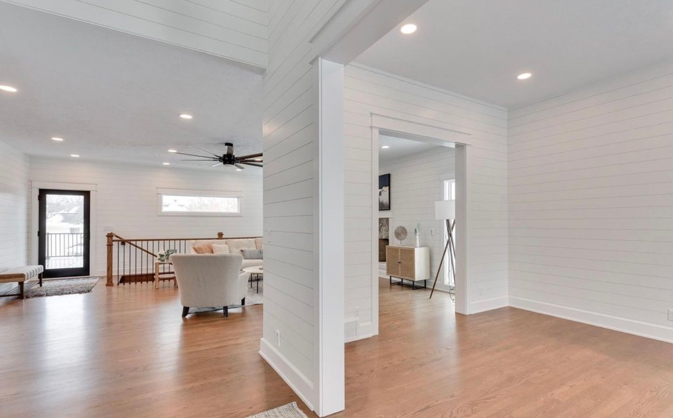 Bright open living room with hardwood floors, white walls, and a dining area visible through a large doorway