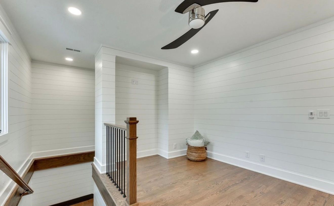 Bright white upstairs landing with wood floor, ceiling fan, and stair railing