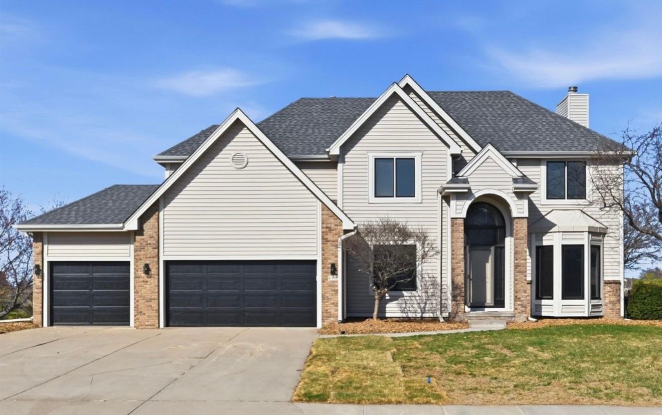 Suburban two-story house with three-car garage, gray siding, brick accents, and front lawn