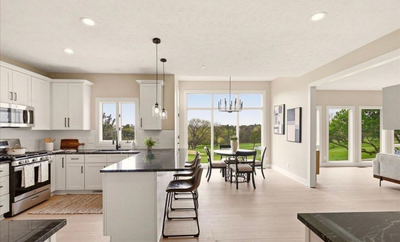 Bright modern kitchen and dining area with white cabinets, island, and large windows overlooking greenery