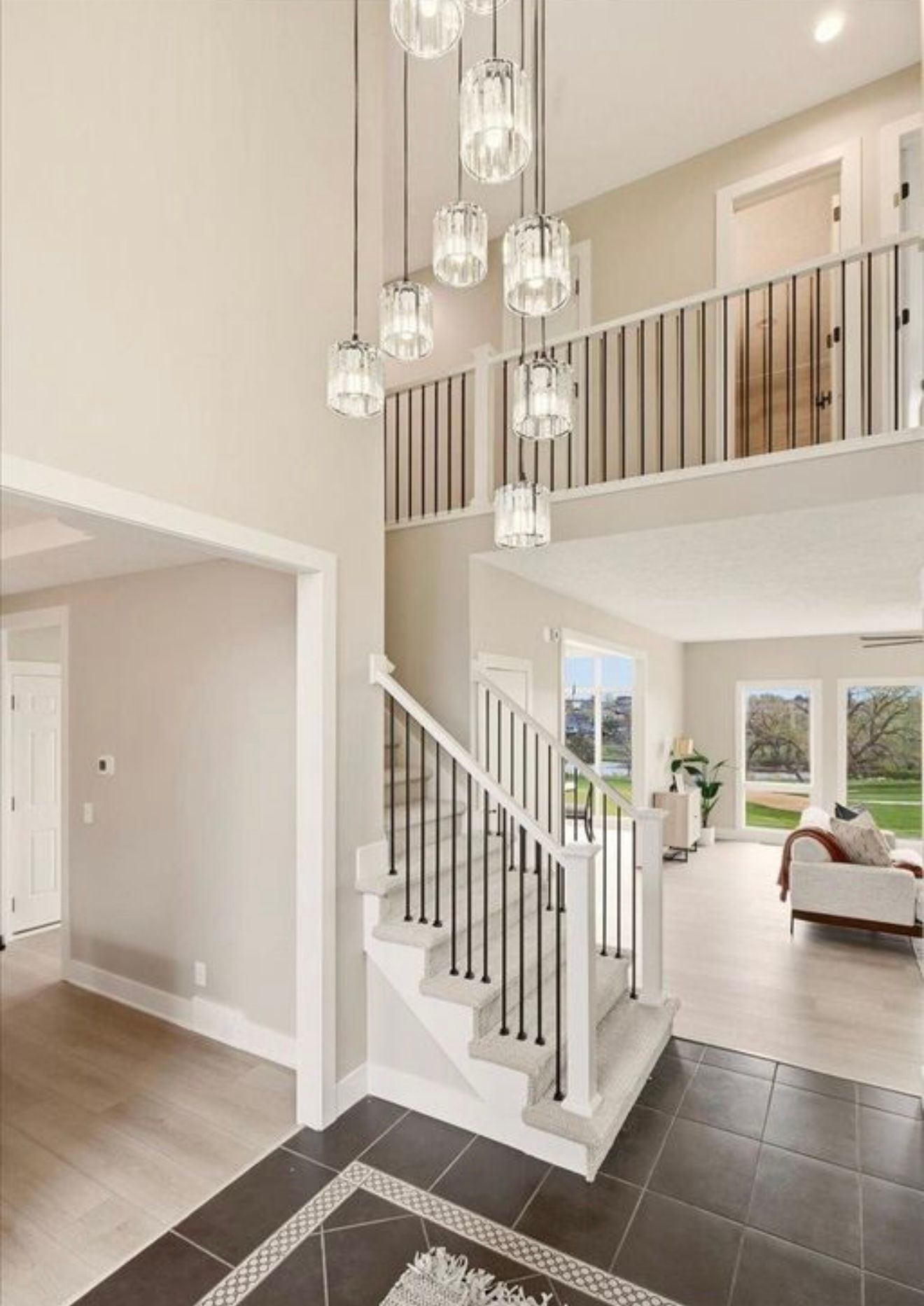 Modern foyer with black tile floor, white staircase, and glass pendant lights opening to a bright living room