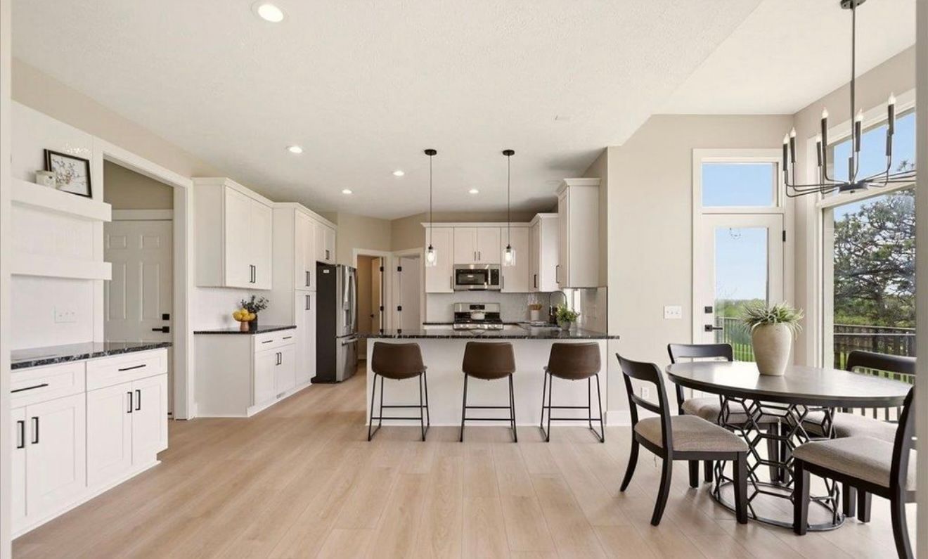 Bright open kitchen and dining area with white cabinets, island seating, and large windows.