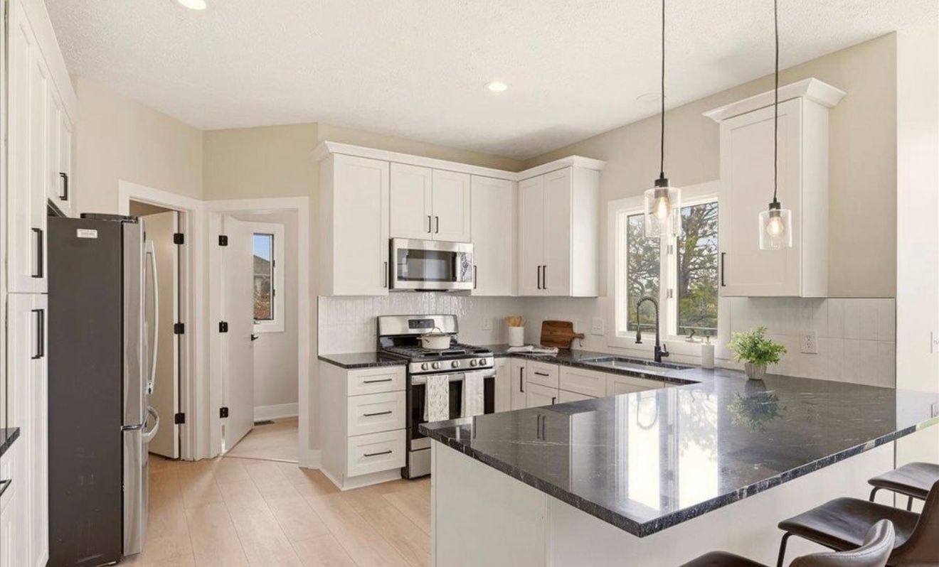 Bright modern kitchen with white cabinets, stainless appliances, and a dark granite island.