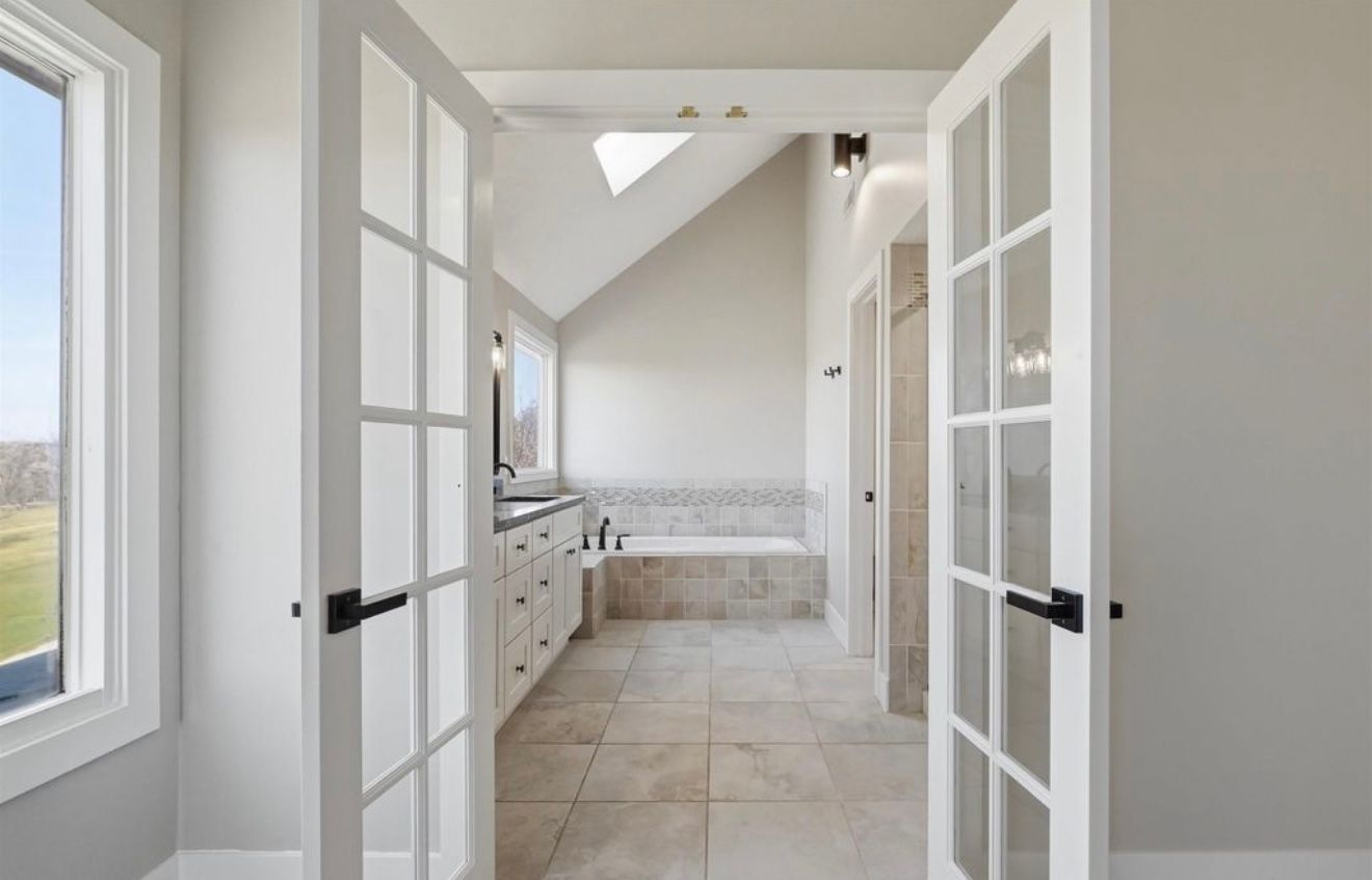 Open French doors framing a bright, beige tiled hallway with a skylight and built-in cabinets.