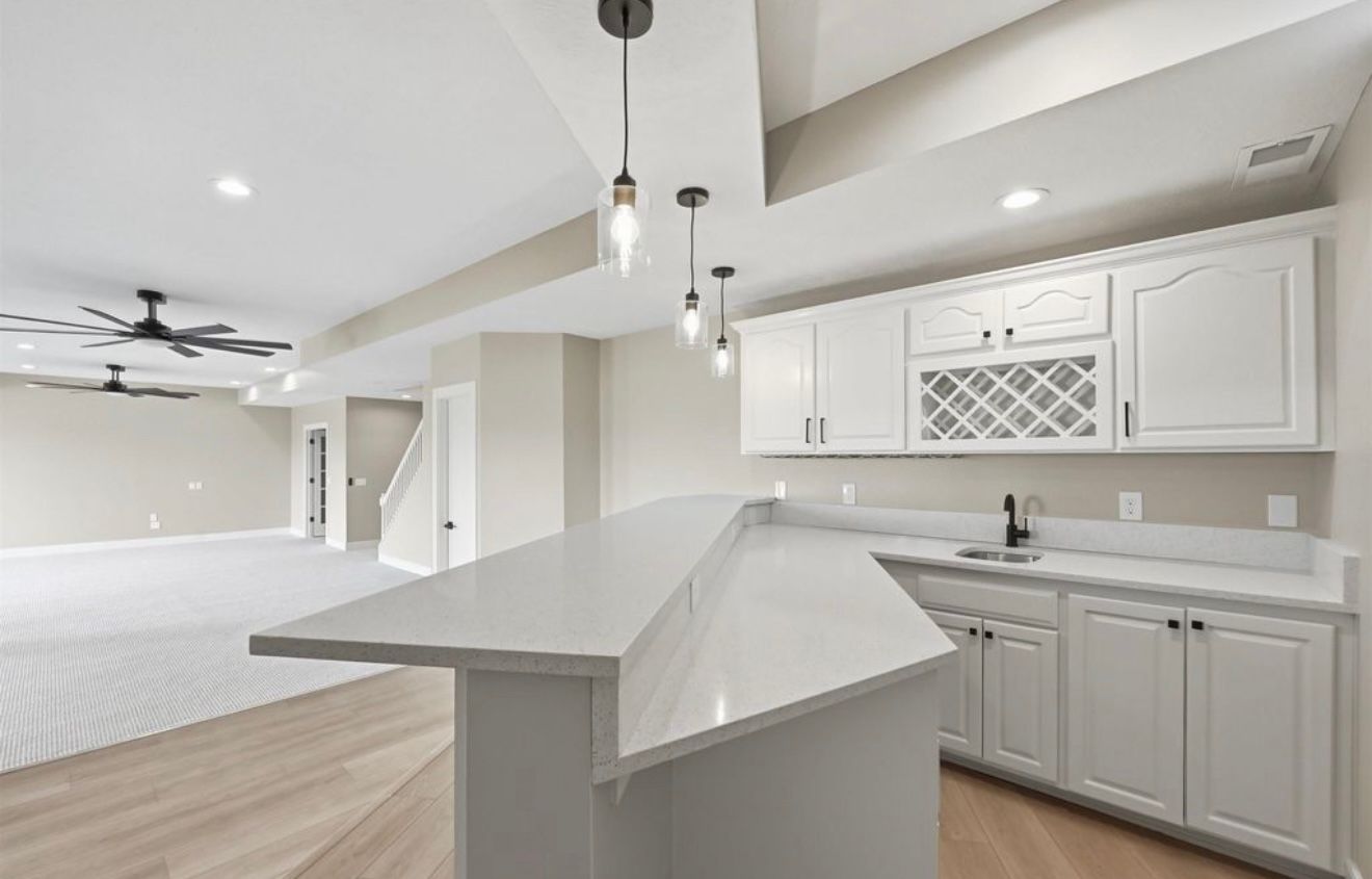 Bright open kitchen with white cabinets, light wood floors, and a central island under pendant lights