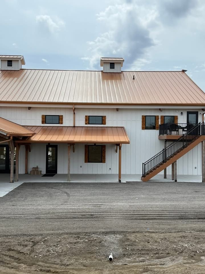 White barn-style building with a metal roof, covered porch, and exterior staircase under a cloudy sky