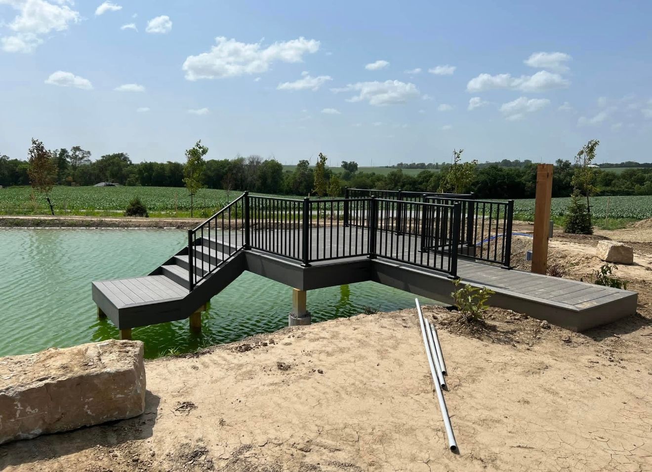 Small metal footbridge over a green pond in a sunny outdoor park setting