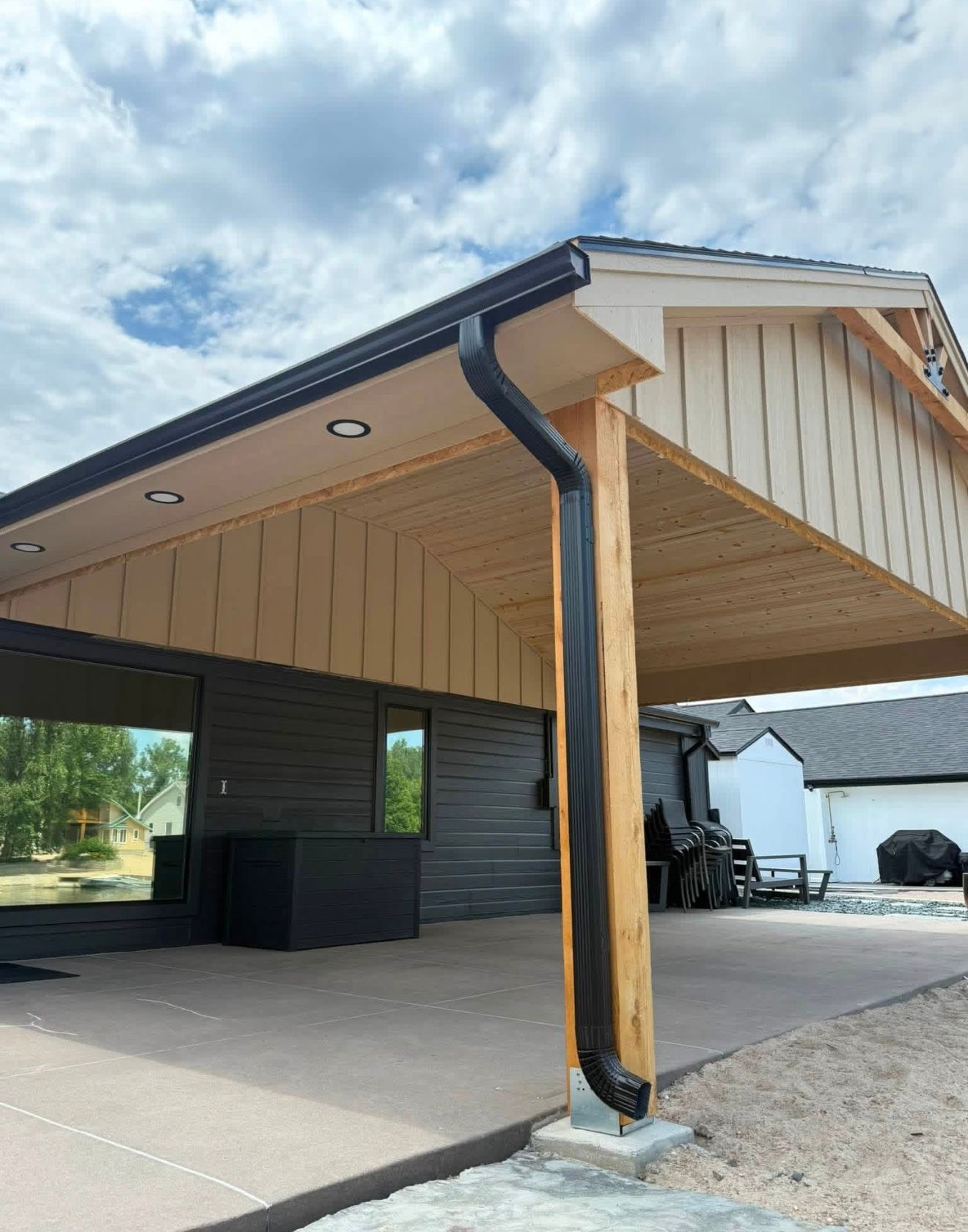 Modern house carport with wood post, black gutter, and concrete driveway under a cloudy sky