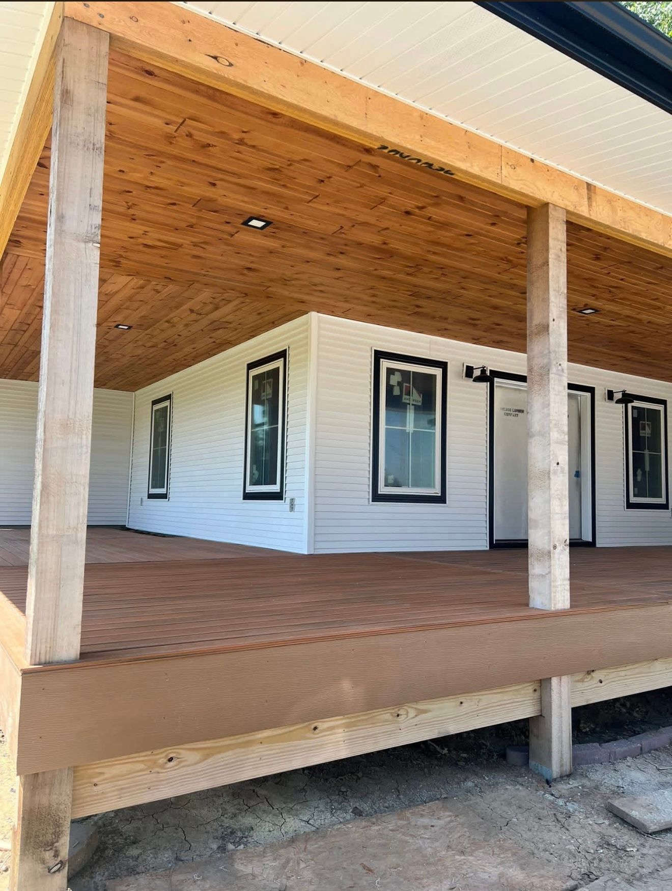 Covered porch with wooden ceiling, white siding, and brick flooring on a house exterior.