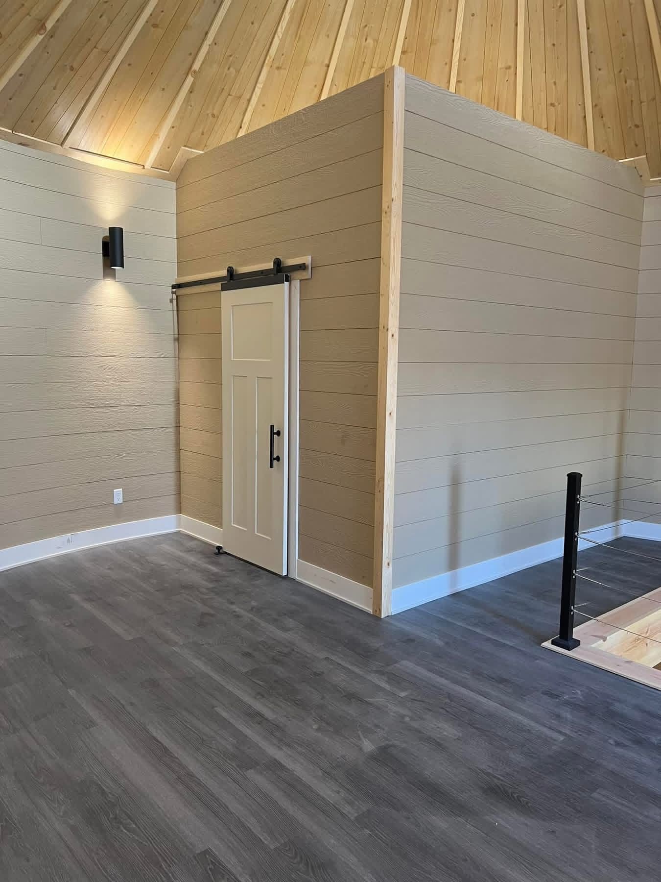 Modern interior with a small door, wood walls, vaulted ceiling, and gray flooring in a spacious room