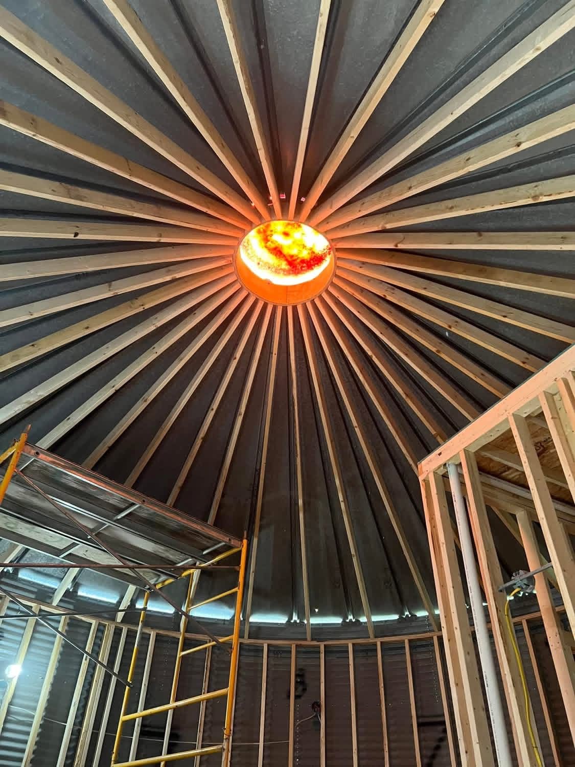 Circular domed ceiling with radial beams and a glowing orange light at the center, above a construction area