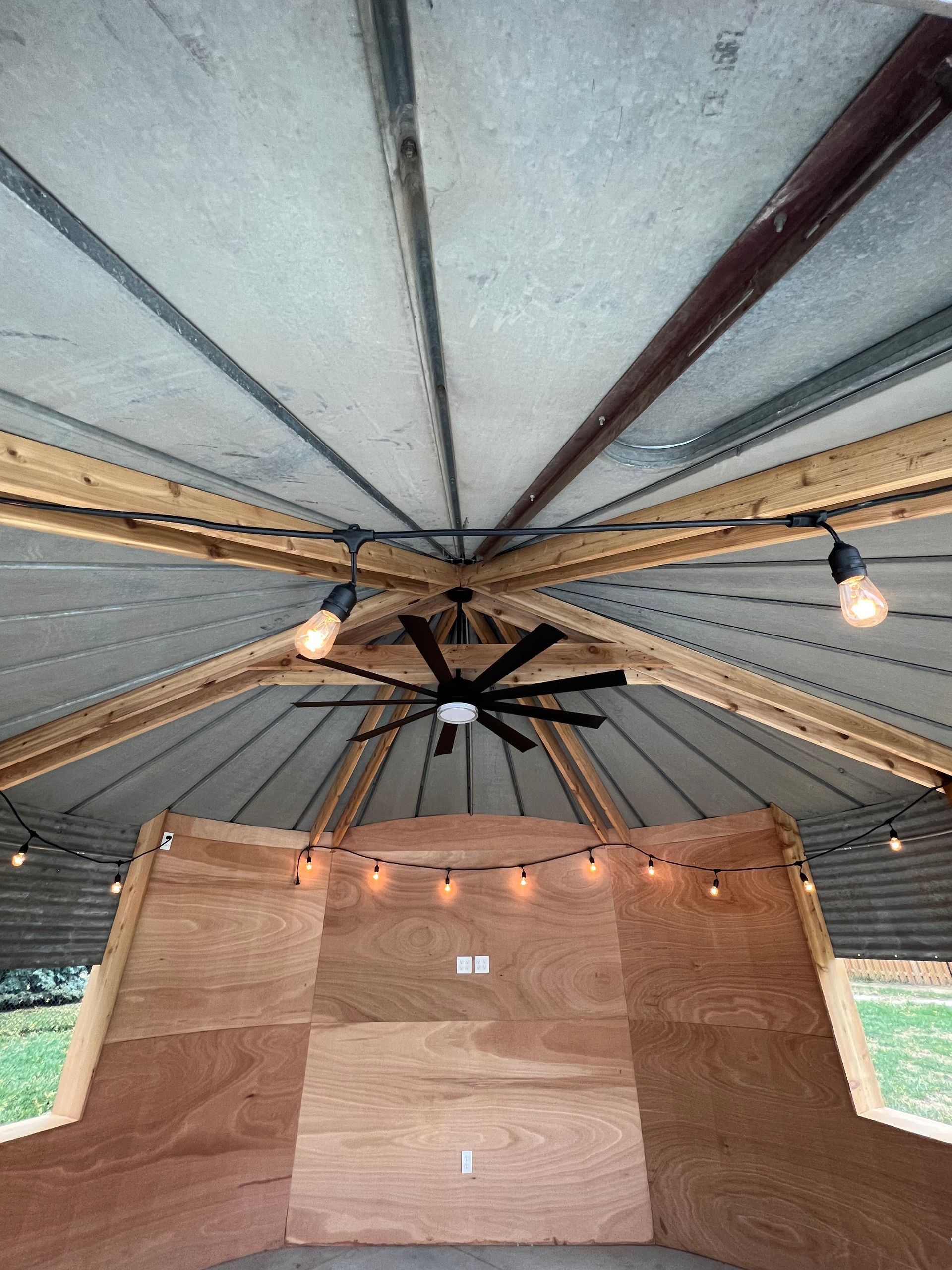 Ceiling of a rustic tent with exposed beams, string lights, and wooden wall panels below.