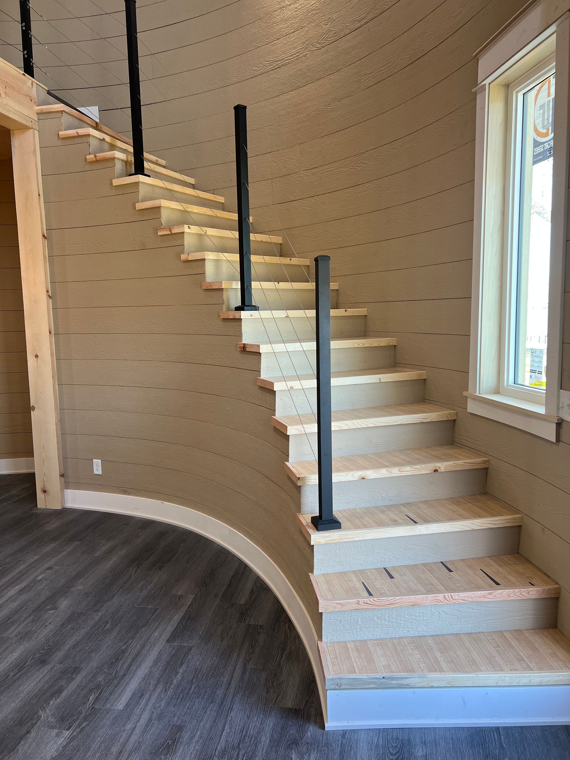 Curved staircase with white steps and black railings inside a bright room with a window