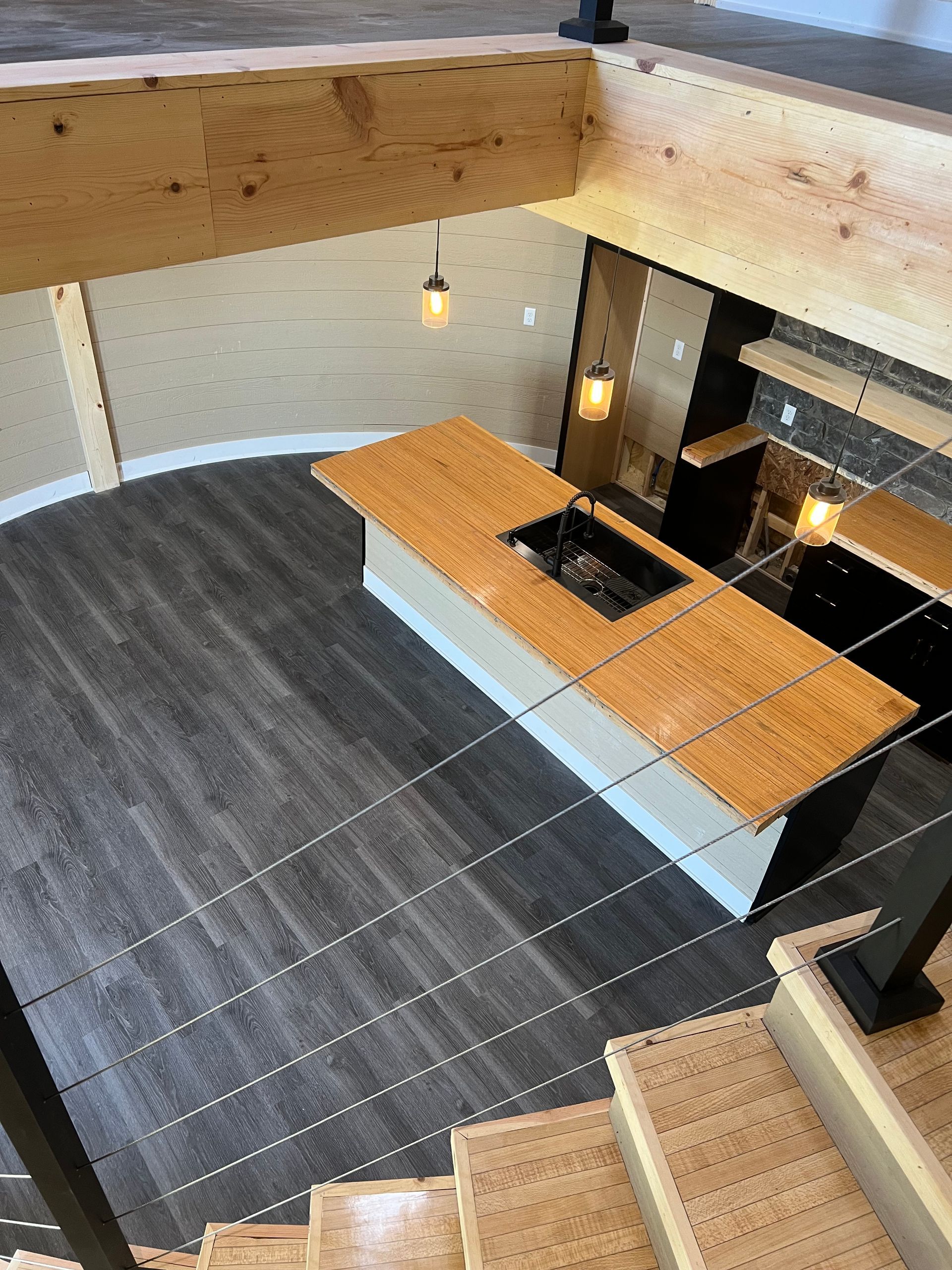 Modern loft interior with open staircase, gray tile floor, wooden beam, and black kitchen island