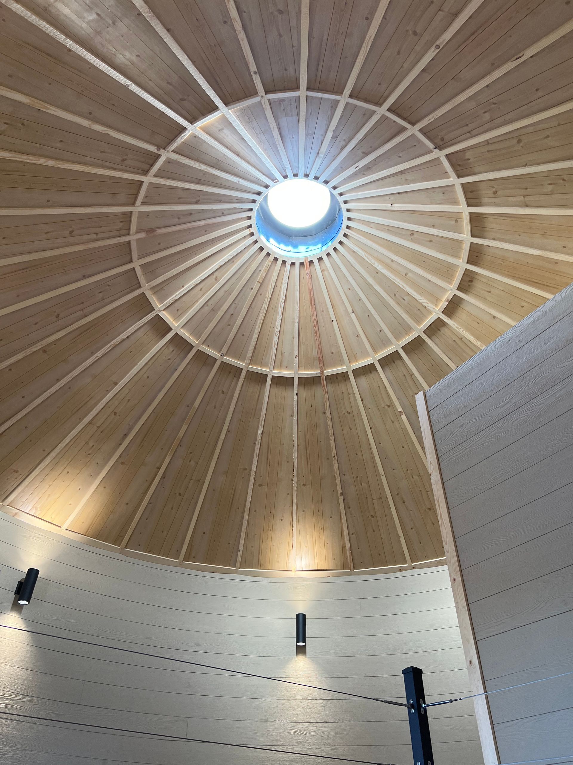 Wooden domed ceiling with a central skylight above a modern interior wall.