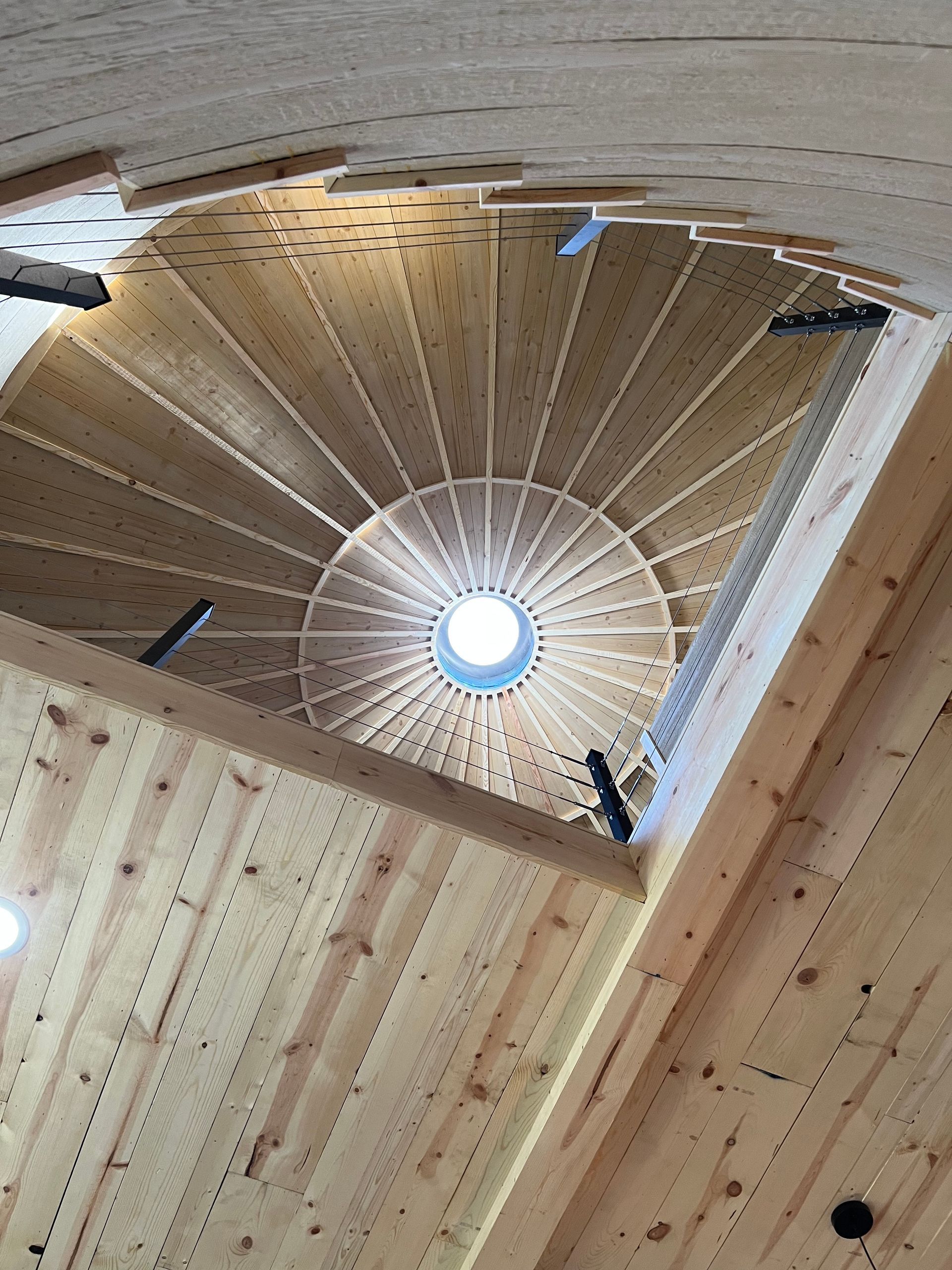 Spiral wooden staircase viewed from below, with a skylight at the center.