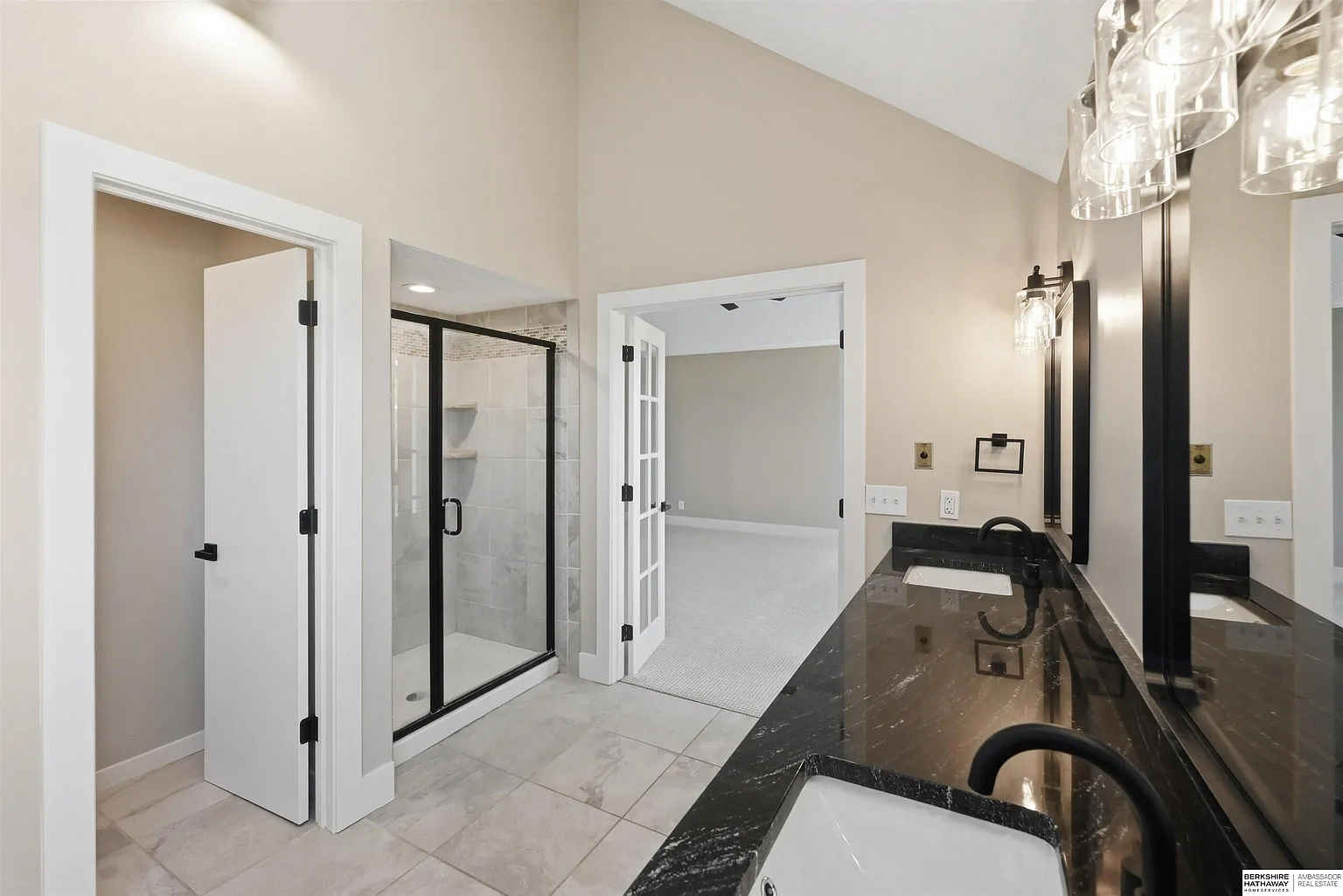 Modern bathroom vanity with black countertop, glass shower, and white doors in a bright neutral room