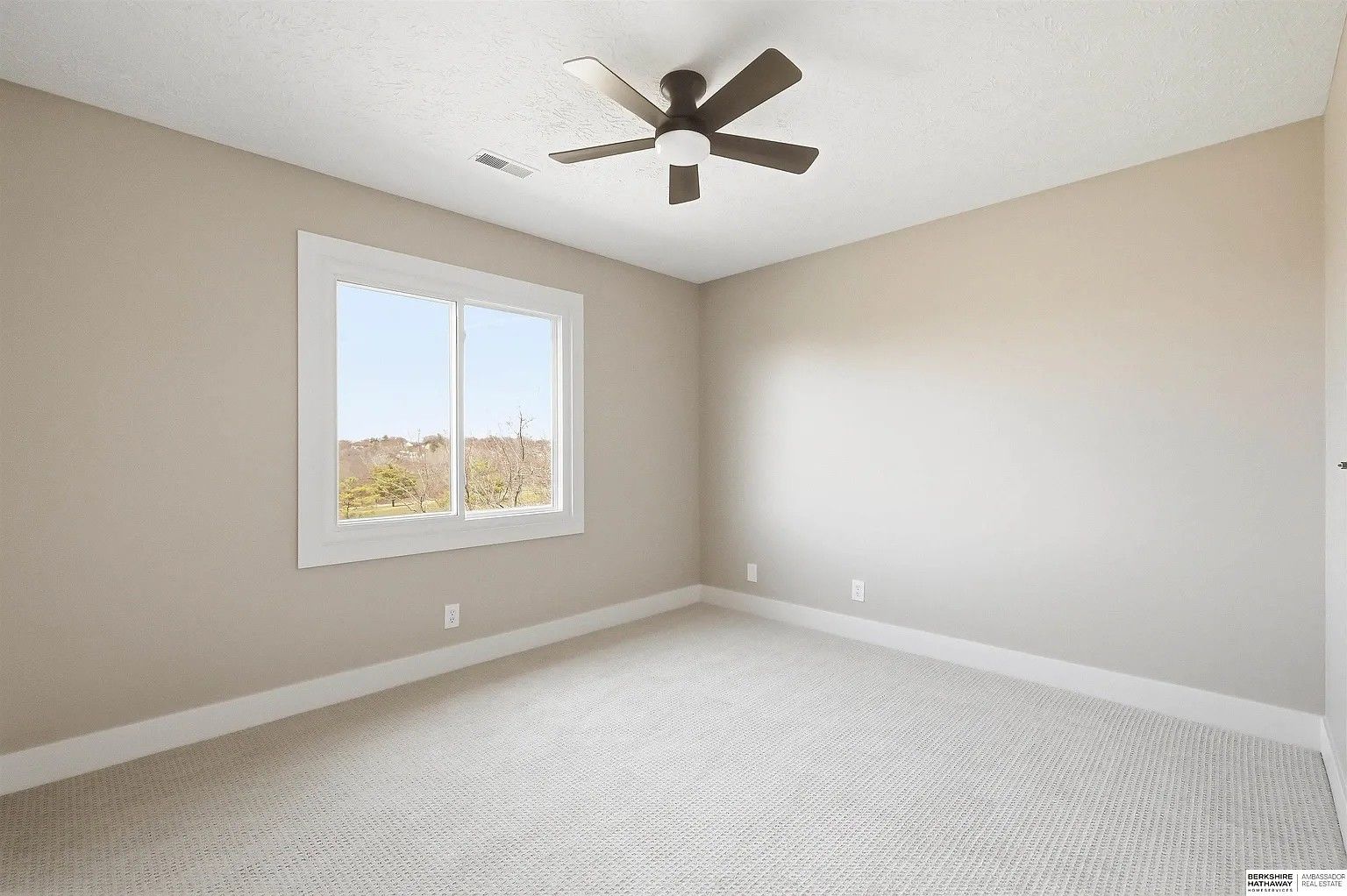 Empty beige bedroom with white carpet, a ceiling fan, and a window letting in natural light