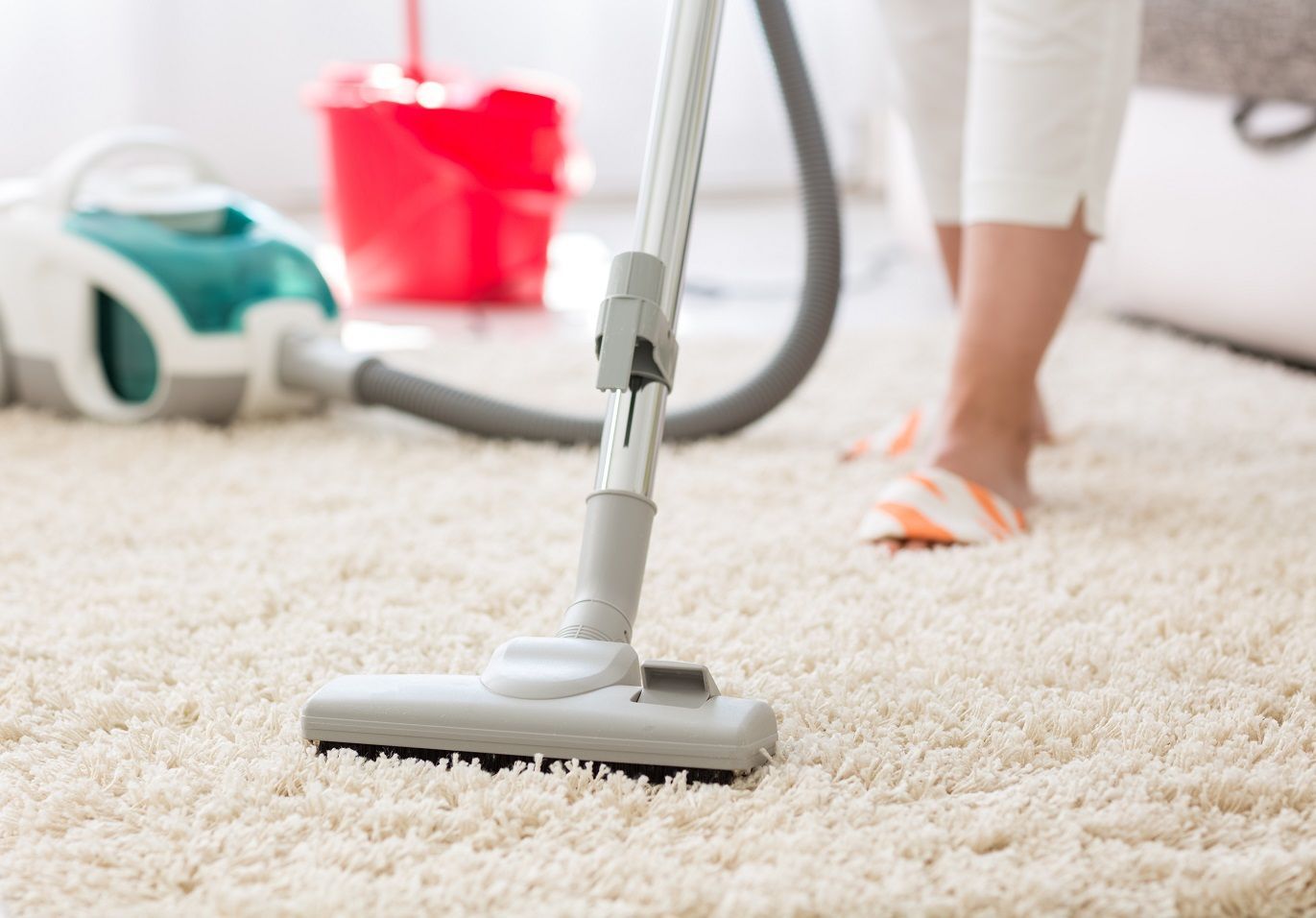 Vacuum cleaner on a white carpet with a person cleaning in the background