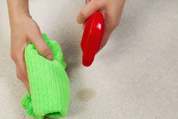Hands cleaning with a green cloth and red spray bottle on a beige surface