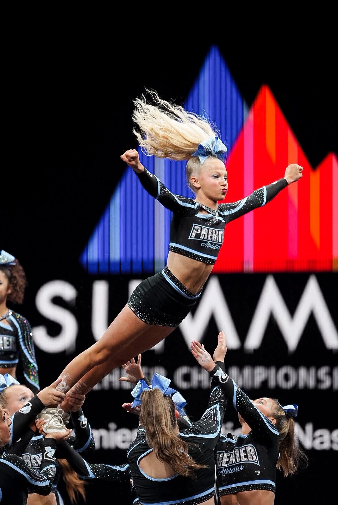A cheerleader is being lifted in the air by two other cheerleaders