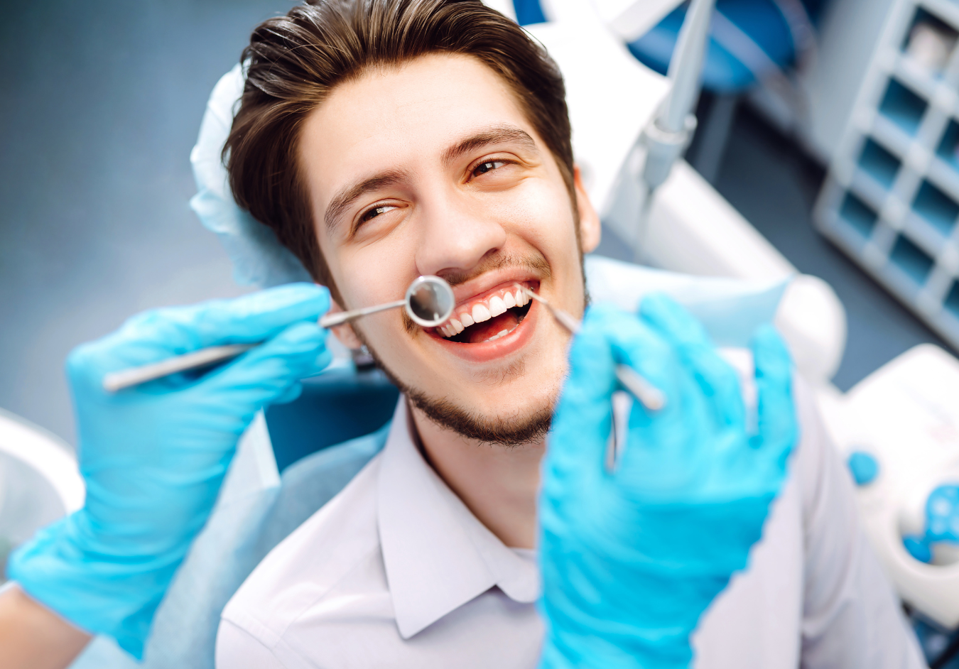 Man smiling at dentist during a check-up. Dentist in blue gloves holding dental tools.