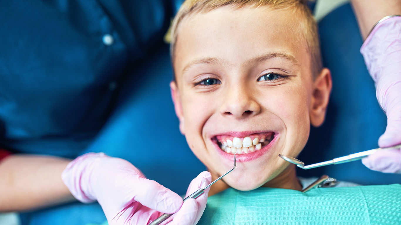 Boy at a dental check-up smiles while a dentist uses tools in his mouth.