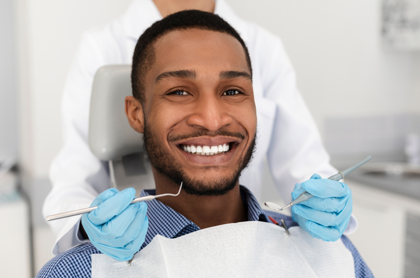 Man smiling at the dentist, seated in a dental chair, holding dental tools, wearing blue gloves.