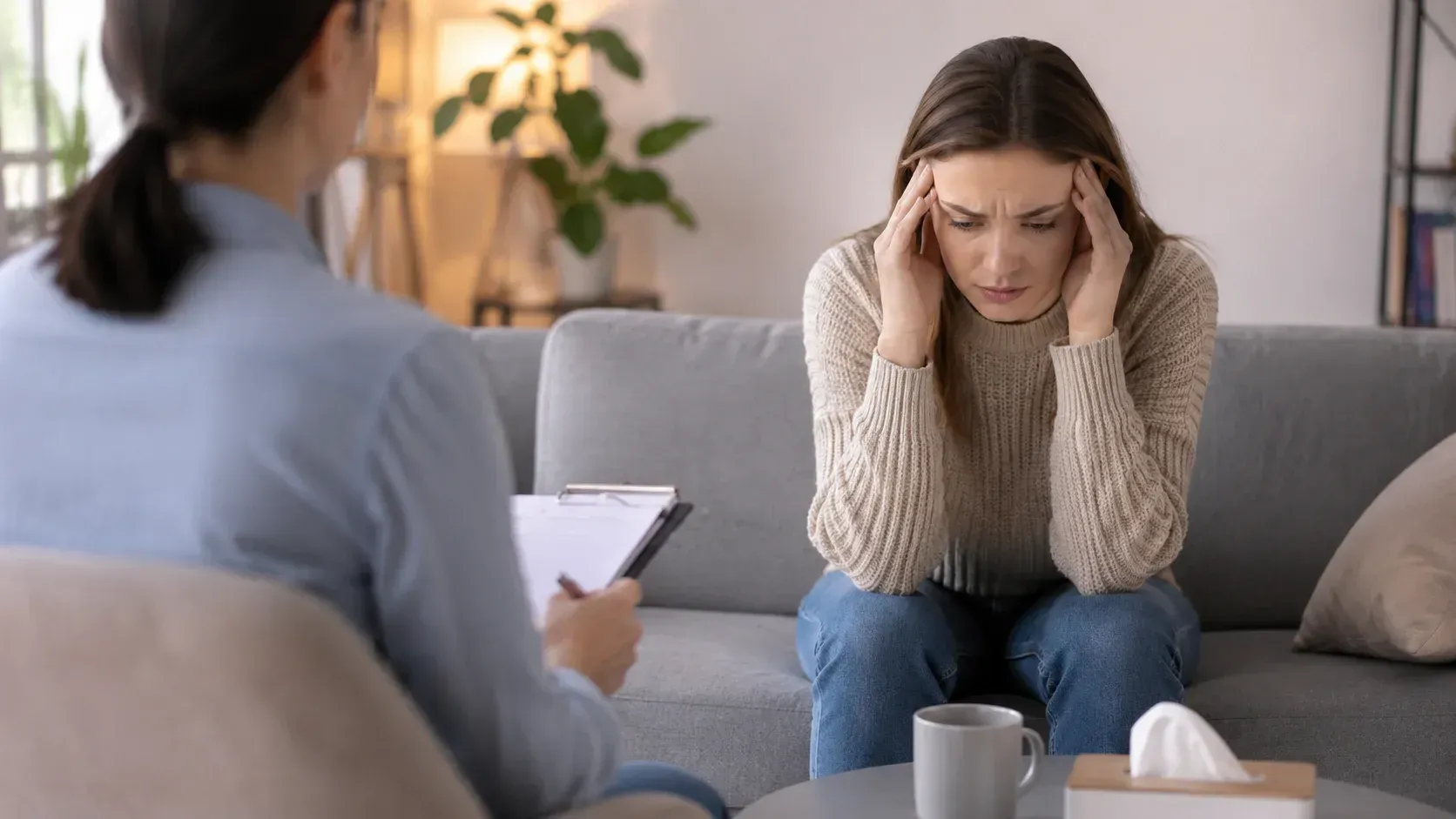 A woman holding her head in distress speaks with her therapist in a office during a session.
