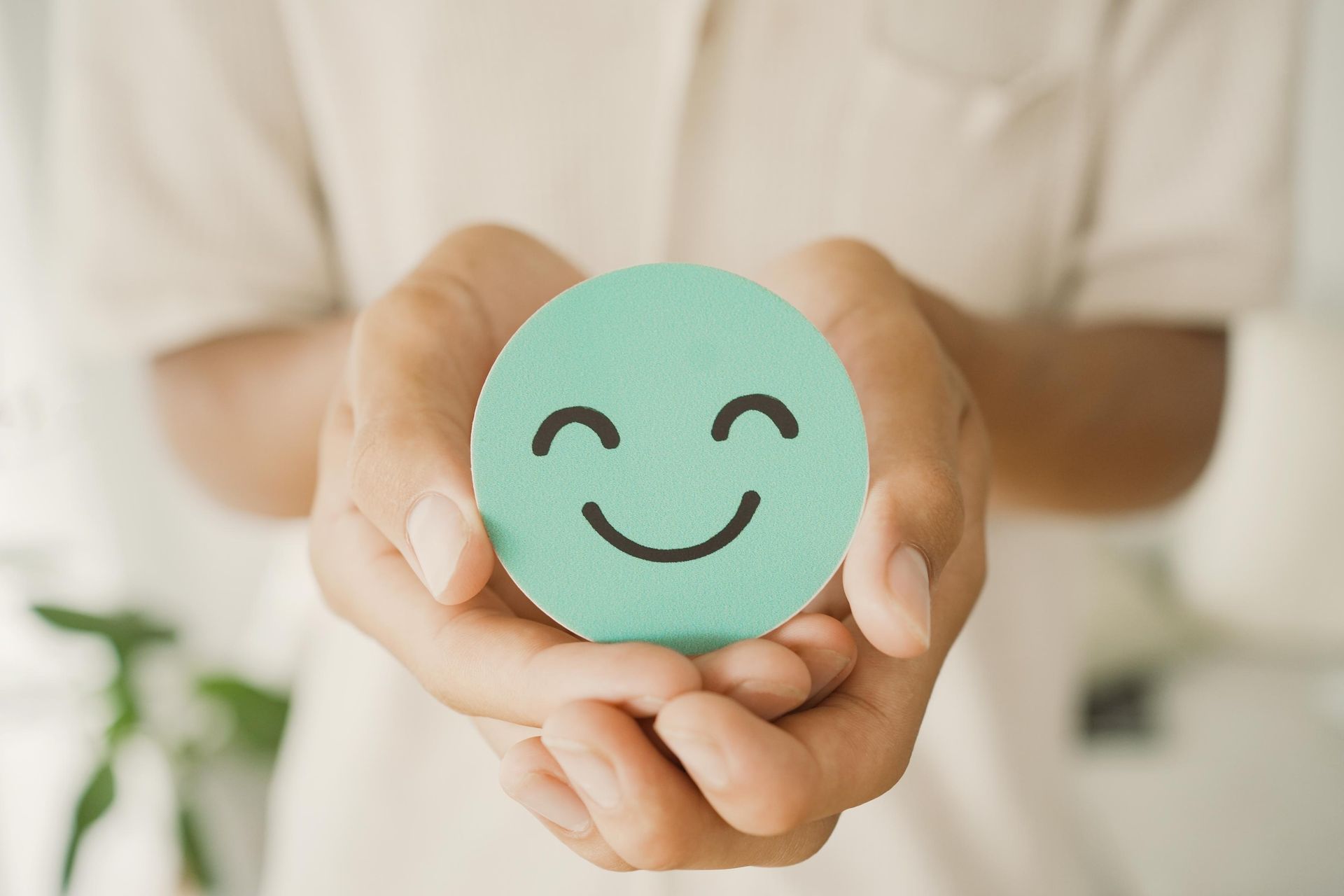 Hands holding a round, light teal paper with a smiling face drawn on it.