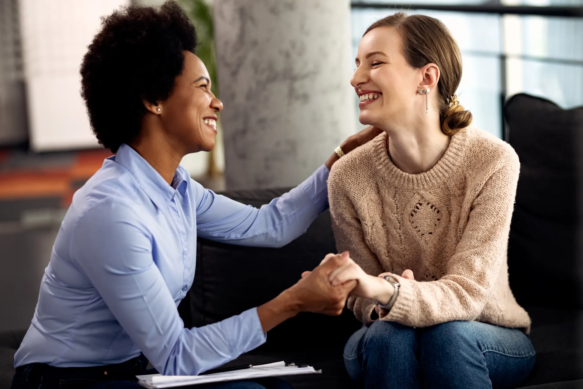 Two people sitting close, smiling and holding hands in a warm indoor setting